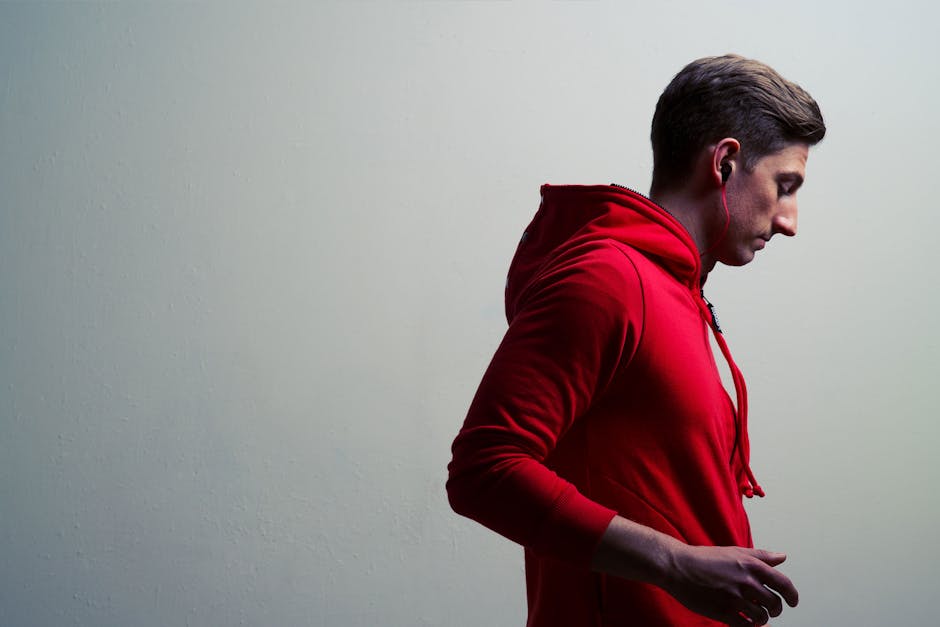 battery heated hoodie technology - Side profile of a young man wearing a red hoodie and earphones against a minimalist background.