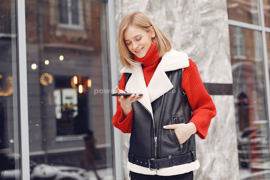 heated sweater technology - A woman in winter clothing smiles while holding a smartphone outside a glass window.
