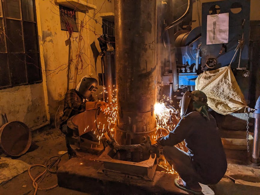 electric heated jacket - Workers welding a large metal pipe, creating sparks in a Dhaka workshop. Industrial atmosphere.