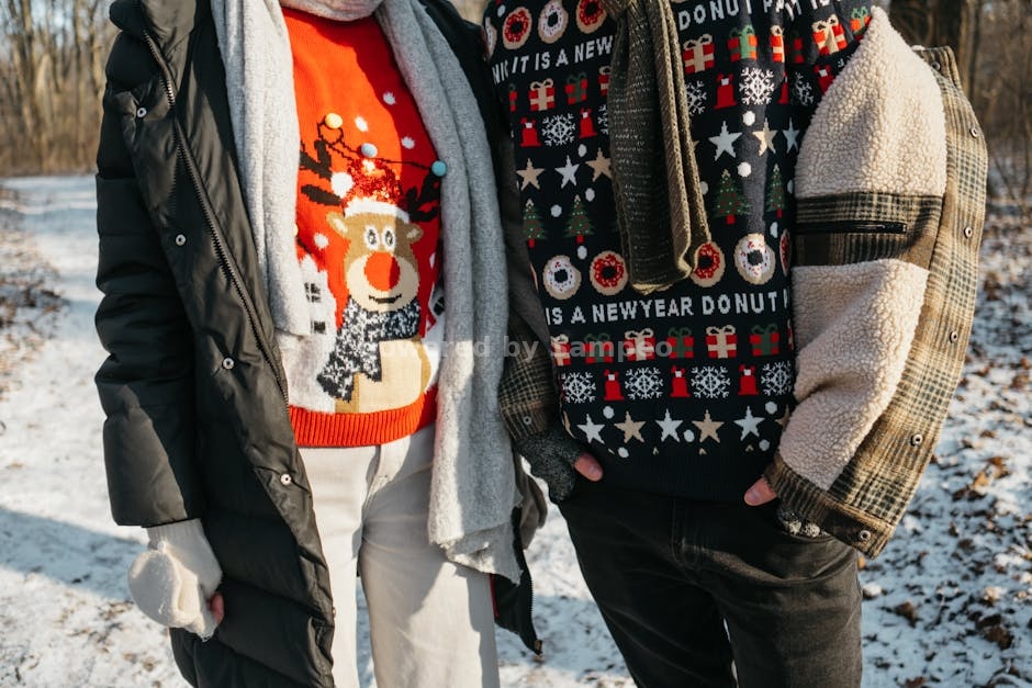 electric heated sweater - Two adults wearing festive Christmas sweaters and winter coats in a snowy outdoor setting.