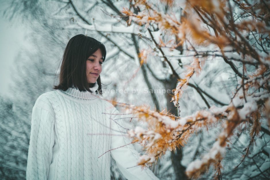 electric heated sweater outdoor activities - A woman in a white sweater stands by a snow-covered tree in winter. Outdoor fashion photography in Ukraine.