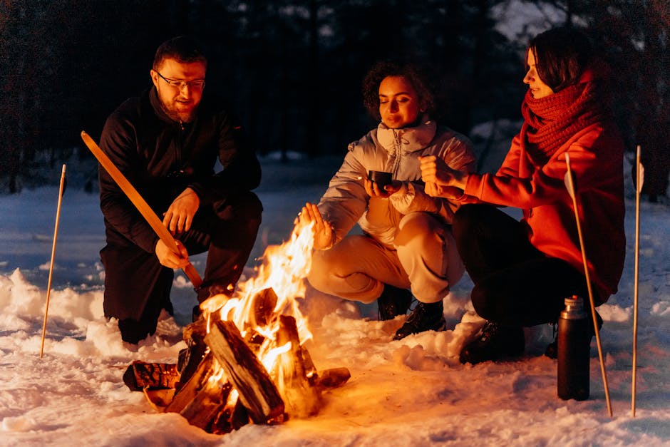 heated garments outdoor activities - People enjoying warmth by a campfire in a snowy landscape during a winter evening.