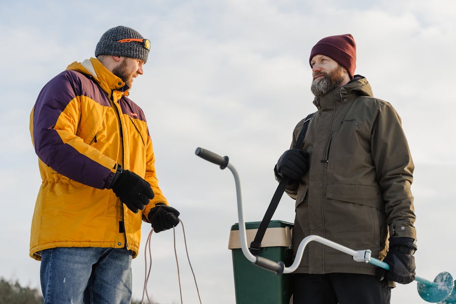 heated jacket outdoor activities - Two bearded men in winter clothes ice fishing outdoors with equipment.